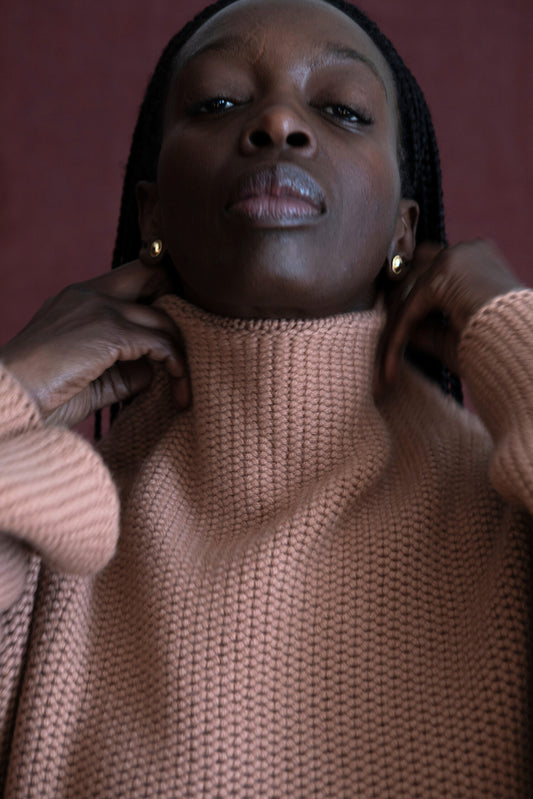 This image features a model wearing the Mousse Sweater, an oversized chunky knit blanket sweater made from 100% Mongolian cashmere. The sweater comes in a soft, muted shade of beige, enhancing its cozy and comforting appearance.
