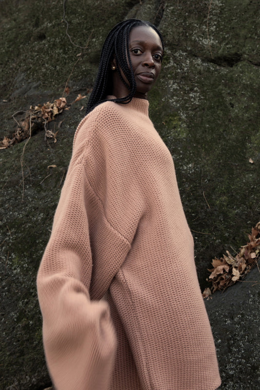 This image features a model wearing the Mousse Sweater, an oversized chunky knit blanket sweater made from 100% Mongolian cashmere. The sweater comes in a soft, muted shade of beige, enhancing its cozy and comforting appearance.