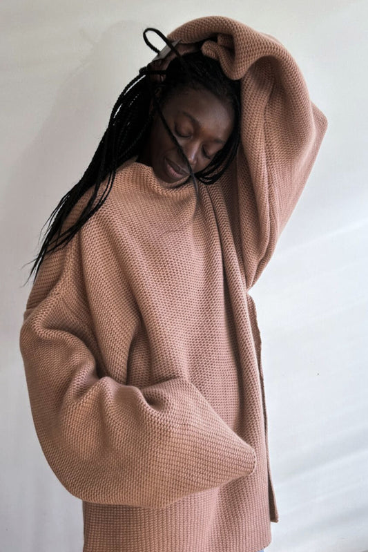 This image features a model wearing the Mousse Sweater, an oversized chunky knit blanket sweater made from 100% Mongolian cashmere. The sweater comes in a soft, muted shade of beige, enhancing its cozy and comforting appearance.