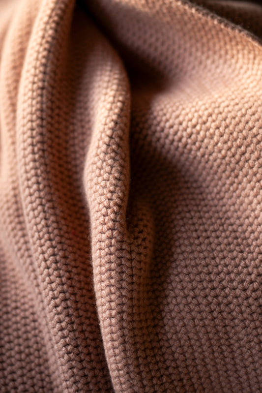 This image features a model wearing the Mousse Sweater, an oversized chunky knit blanket sweater made from 100% Mongolian cashmere. The sweater comes in a soft, muted shade of beige, enhancing its cozy and comforting appearance.