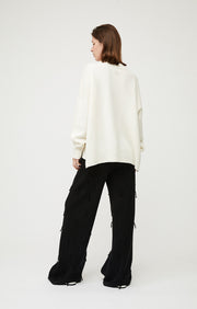Woman wearing Alia oversized fit cashmere sweater in colour Ivory.  The cashmere sweater is knitted in a single jersey stitch. 