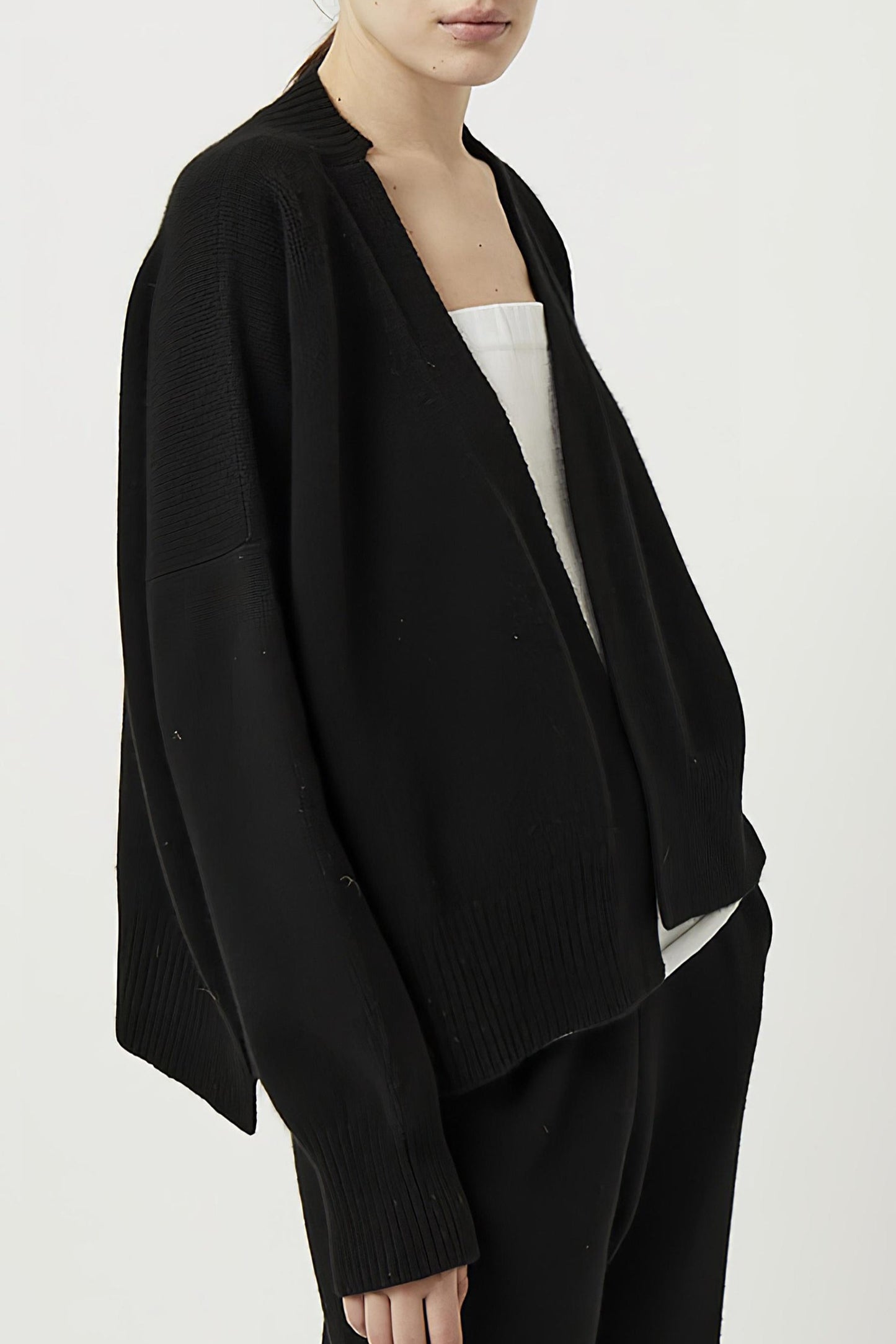 This image features the Aire Cardigan, a luxurious, chunky open cardigan made from pure cashmere. The cardigan is displayed on a model, showcasing its sleek black color and stylish design elements.