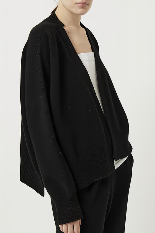 This image features the Aire Cardigan, a luxurious, chunky open cardigan made from pure cashmere. The cardigan is displayed on a model, showcasing its sleek black color and stylish design elements.