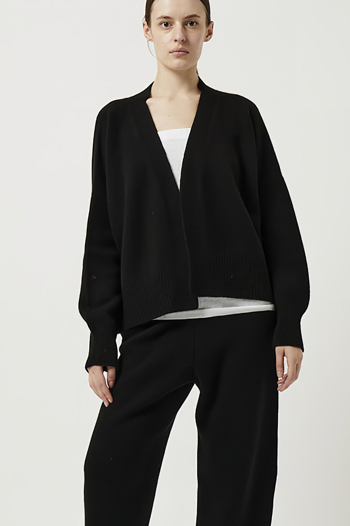 This image features the Aire Cardigan, a luxurious, chunky open cardigan made from pure cashmere. The cardigan is displayed on a model, showcasing its sleek black color and stylish design elements.