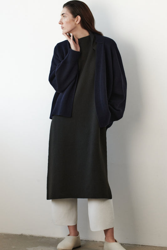 This image features the Aire Cardigan, a luxurious, chunky open cardigan made from pure cashmere. The cardigan is displayed on a model, showcasing its sleek ocean color and stylish design elements.