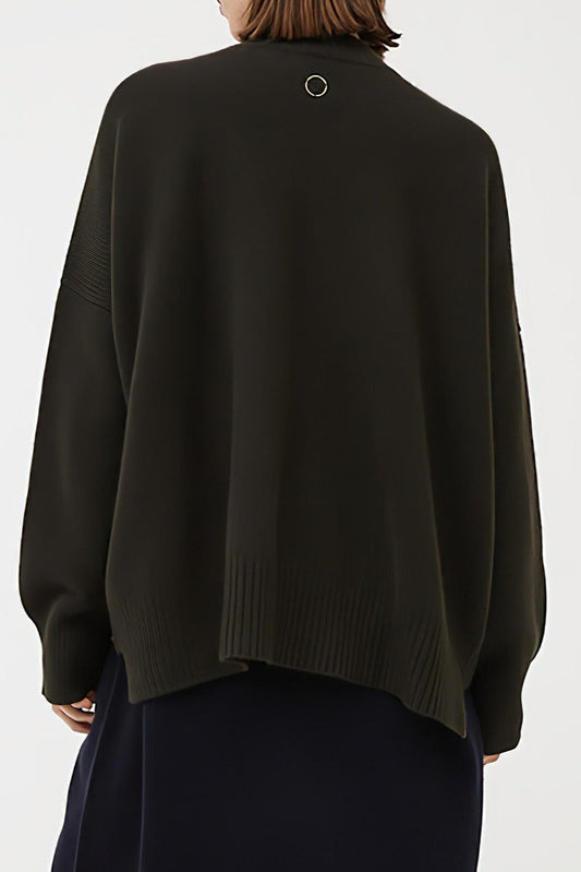 This image features the Aire Cardigan, a luxurious, chunky open cardigan made from pure cashmere. The cardigan is displayed on a model, showcasing its sleek forest color and stylish design elements.