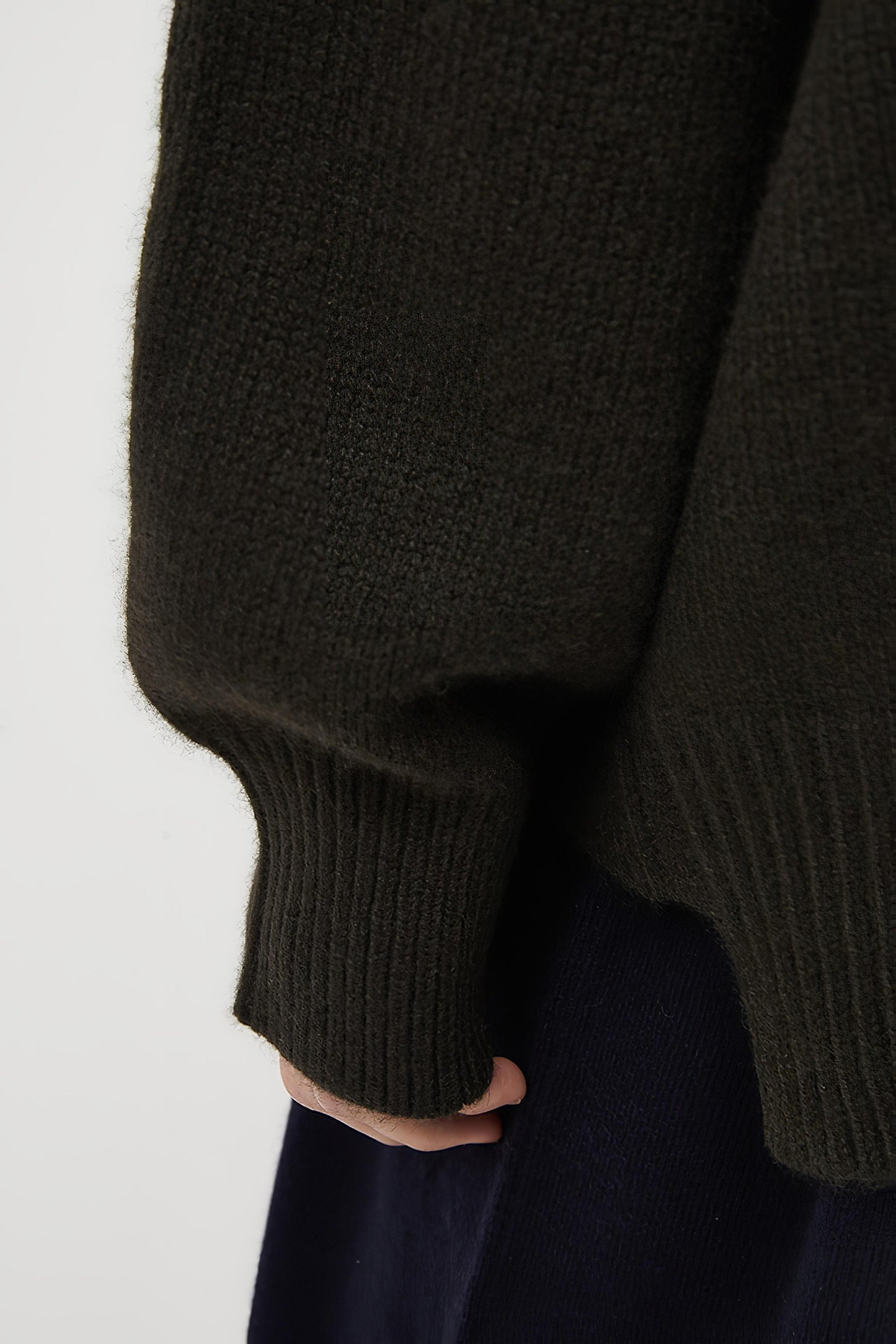 This image features the Aire Cardigan, a luxurious, chunky open cardigan made from pure cashmere. The cardigan is displayed on a model, showcasing its sleek forest color and stylish design elements.