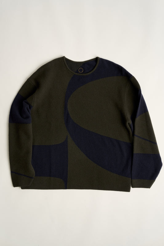 This image features the Arouc Sweater, a stylish and cozy garment that embodies a relaxed, everyday aesthetic. The sweater displays a boxy silhouette, crafted in a knitted jacquard print that forms an abstract, organic pattern in shades of green and navy blue.