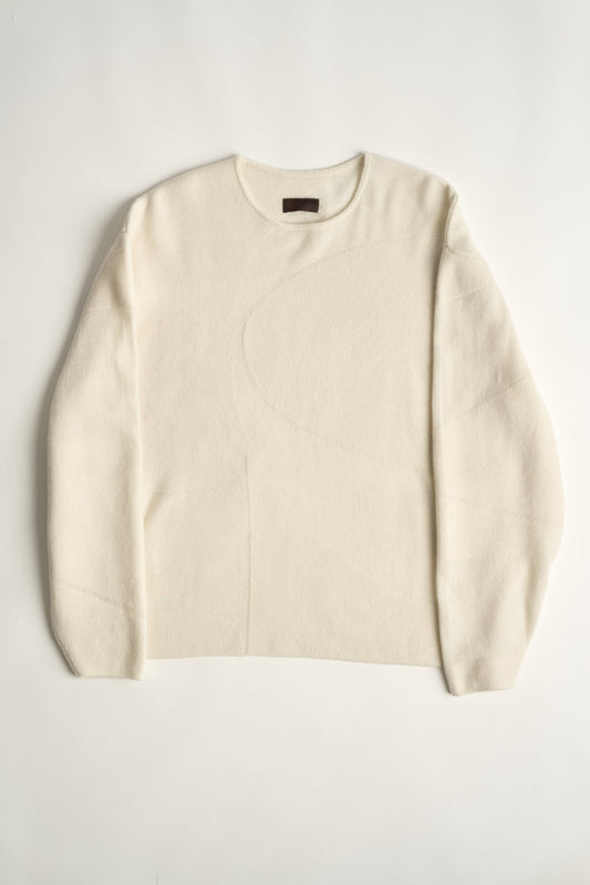 This image features the Arouc Sweater, a stylish and cozy garment that embodies a relaxed, everyday aesthetic. The sweater displays a boxy silhouette, crafted in a knitted jacquard print that forms an abstract, organic pattern in shades of ivory.