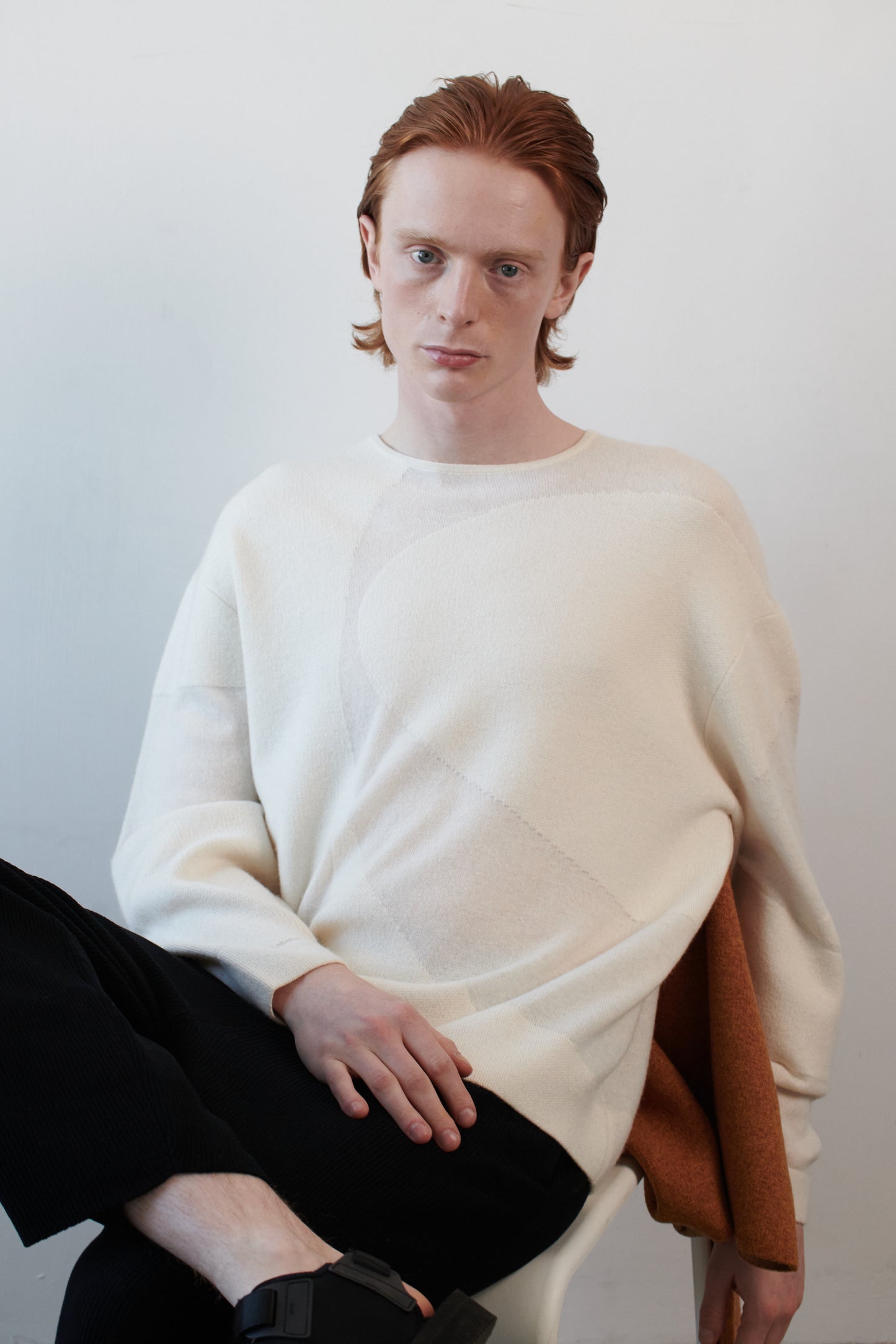 This image features the Arouc Sweater, a stylish and cozy garment that embodies a relaxed, everyday aesthetic. The sweater displays a boxy silhouette, crafted in a knitted jacquard print that forms an abstract, organic pattern in shades of ivory and feather.