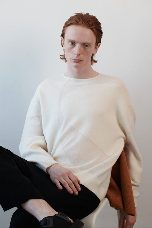 This image features the Arouc Sweater, a stylish and cozy garment that embodies a relaxed, everyday aesthetic. The sweater displays a boxy silhouette, crafted in a knitted jacquard print that forms an abstract, organic pattern in shades of ivory and feather.