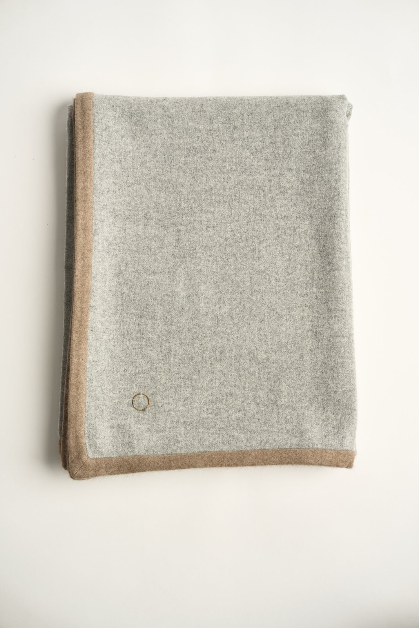 A folded soft grey Arteno throw with a subtle pattern, featuring a small circle detail in the bottom corner.