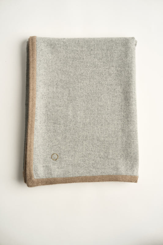 A folded soft grey Arteno throw with a subtle pattern, featuring a small circle detail in the bottom corner.