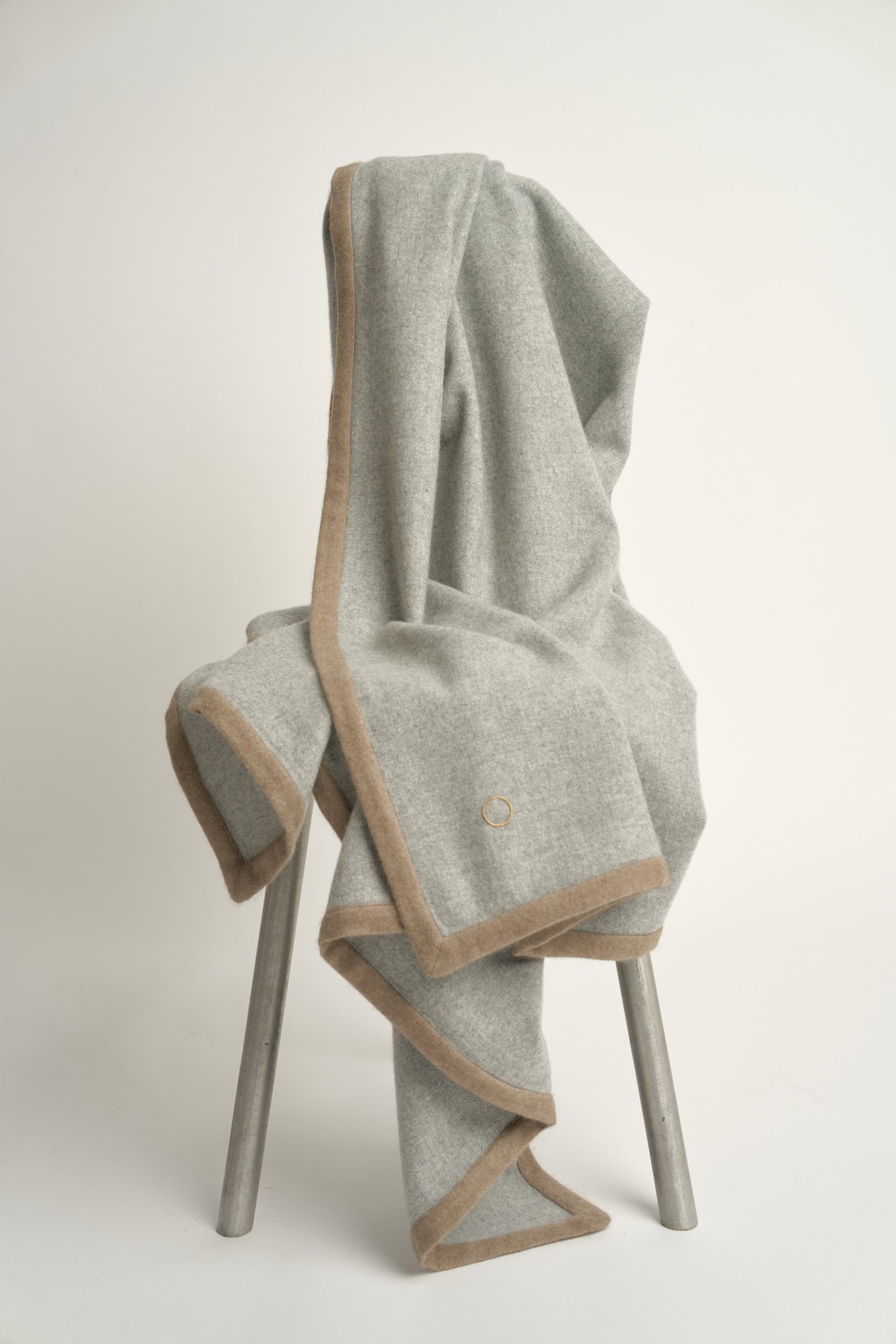 A soft grey Arteno throw with a subtle pattern, featuring a small circle detail in the bottom corner.