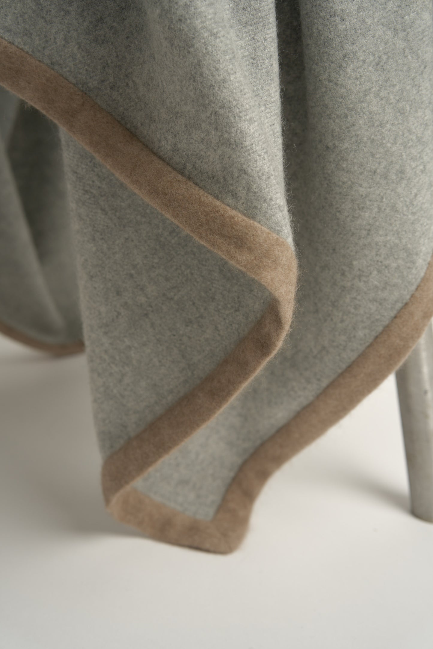 A soft grey Arteno throw with a subtle pattern, featuring a small circle detail in the bottom corner.