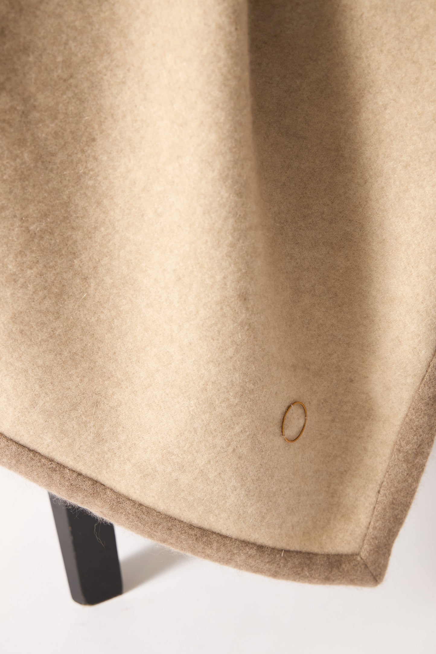 A beige Arteno throw with a subtle pattern and a small circle detail visible on the bottom right corner, displayed on a white background.