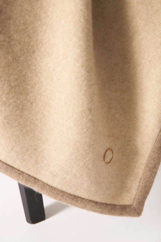 A beige Arteno throw with a subtle pattern and a small circle detail visible on the bottom right corner, displayed on a white background.
