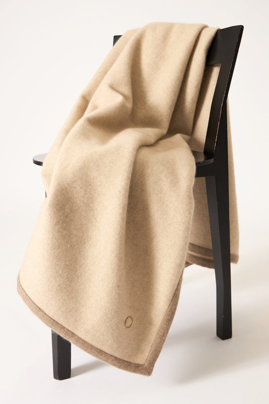 A beige Arteno throw with a subtle pattern and a small circle detail visible on the bottom right corner, displayed on a white background.