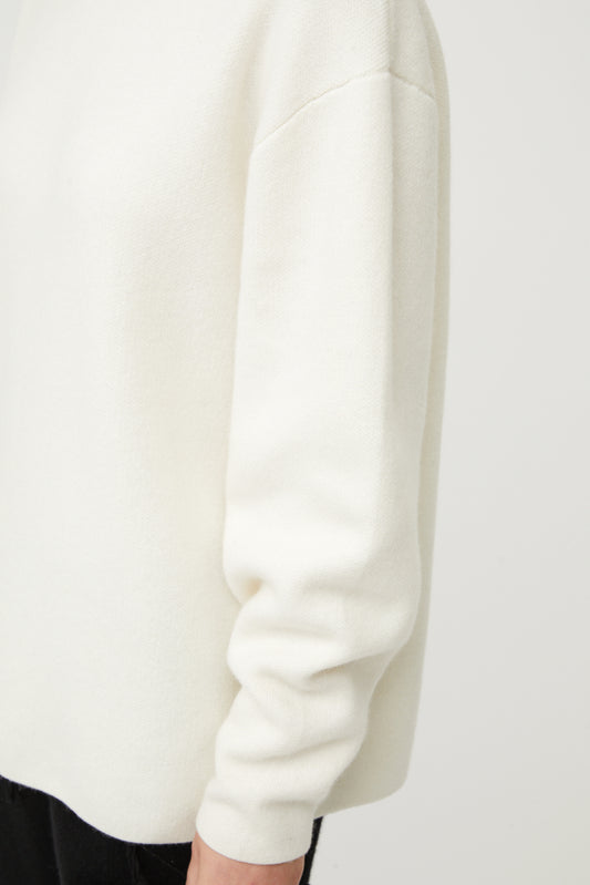 This image features the Axa Sweater, highlighted in a minimalistic style with a ivory color. The sweater showcases an oversized fit with distinct drop shoulders and sculpted, rounded sleeves.