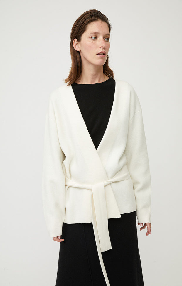 Person wearing Axomi wrap jacket in cashmere in colour Ivory. A relaxed fit jacket with statement sleeves and removable tie belt in cashmere. 