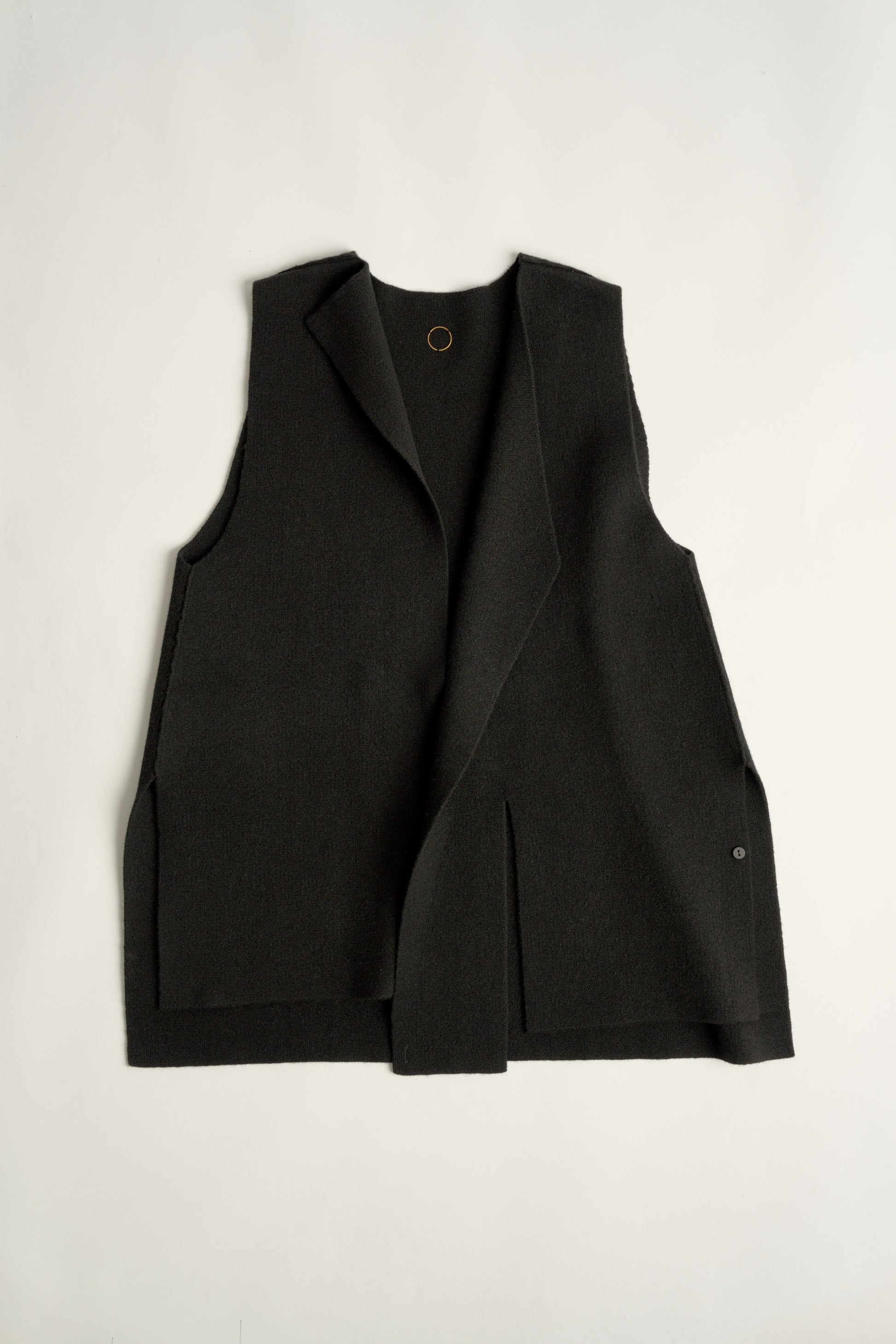 This image features the Ayal Jacket, a stylish sleeveless cashmere jacket displayed on a female model. The jacket is characterized by its asymmetric design, with a distinctive slit on the front left panel and button details on the front hem, adding a touch of uniqueness to its appearance.