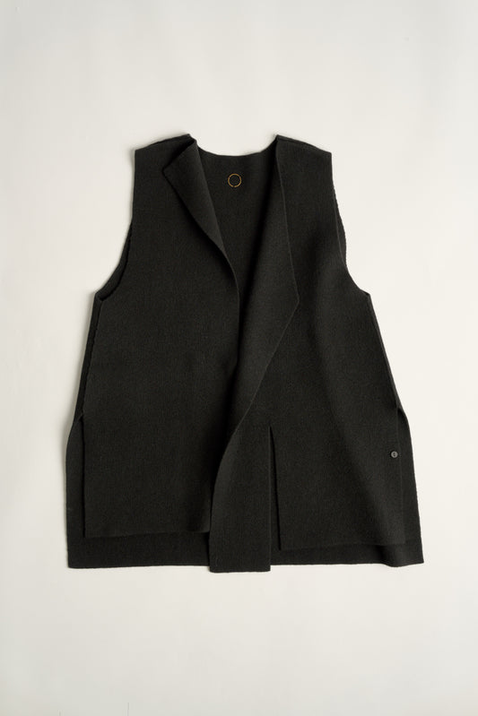 This image features the Ayal Jacket, a stylish sleeveless cashmere jacket displayed on a female model. The jacket is characterized by its asymmetric design, with a distinctive slit on the front left panel and button details on the front hem, adding a touch of uniqueness to its appearance.