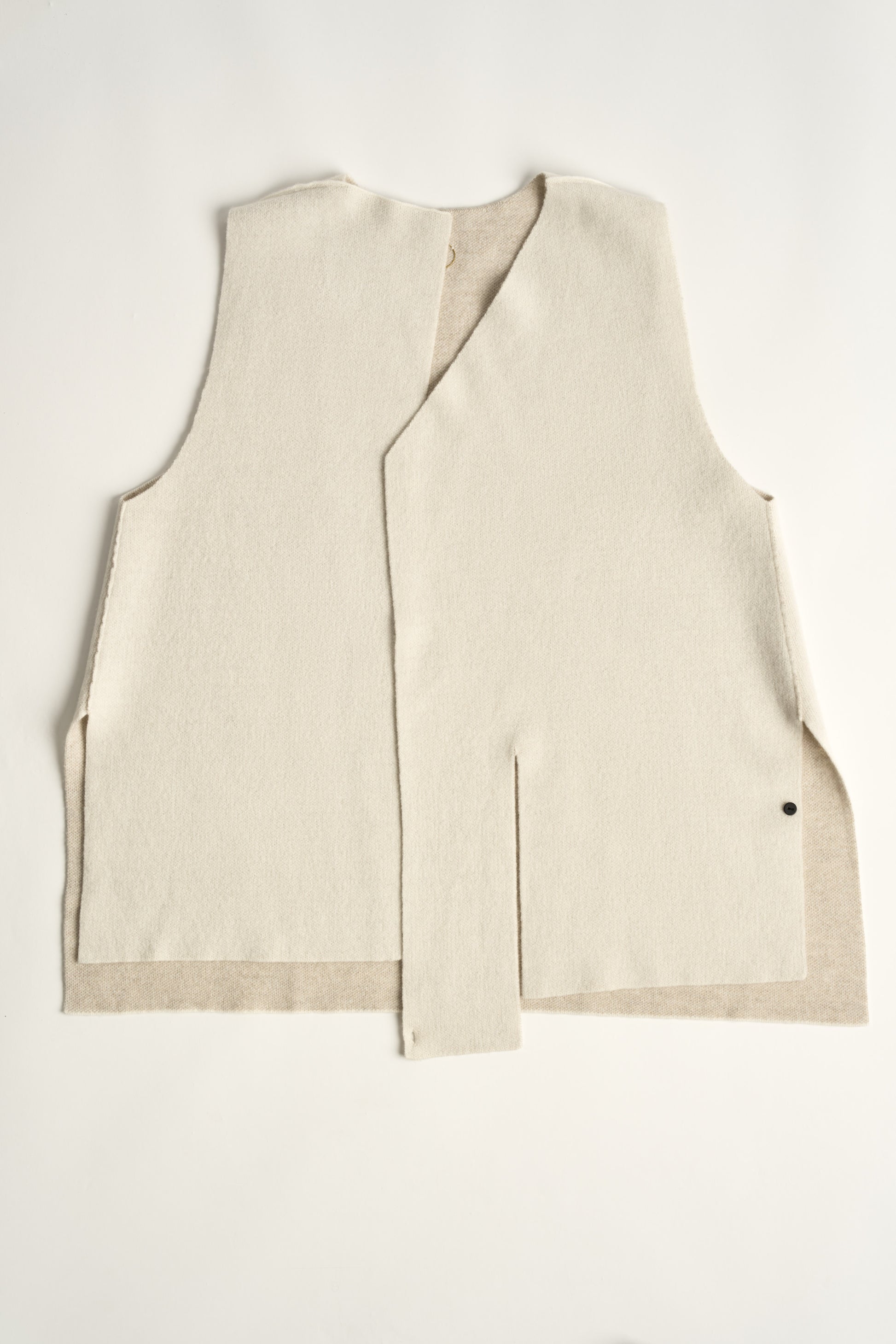 This image features the Ayal Jacket, a stylish sleeveless cashmere jacket displayed on a female model. The jacket is characterized by its asymmetric design, with a distinctive slit on the front left panel and button details on the front hem, adding a touch of uniqueness to its appearance.