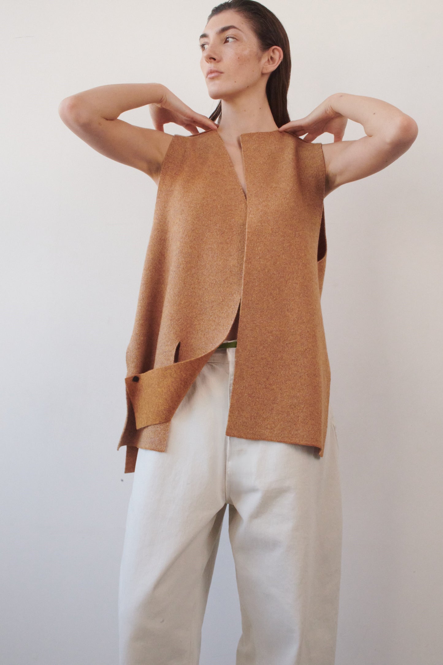 This image features the Ayal Jacket, a stylish sleeveless cashmere jacket displayed on a female model. The jacket is characterized by its asymmetric design, with a distinctive slit on the front left panel and button details on the front hem, adding a touch of uniqueness to its appearance.