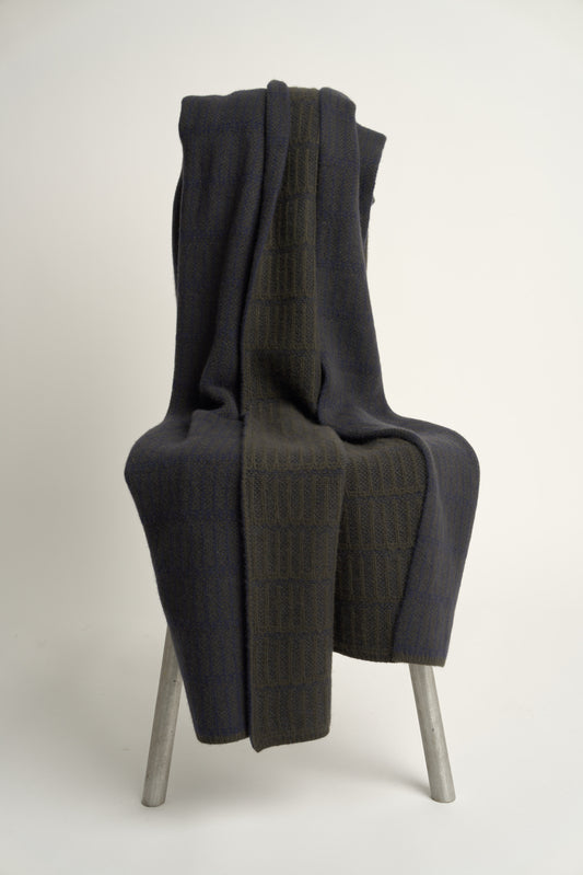A throw blanket with a simple geometric pattern laid out on a flat surface, showcasing alternating vertical lines in two colors.