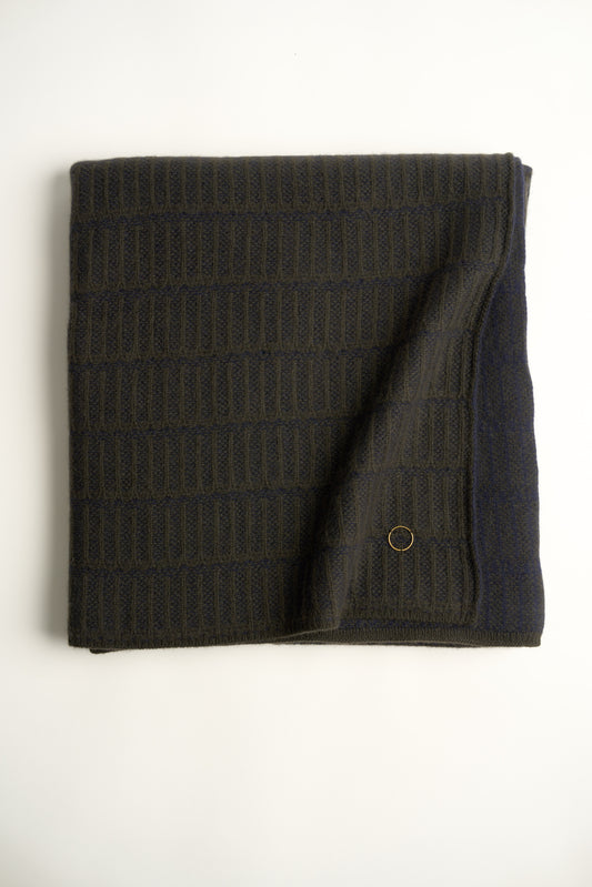 A throw blanket with a simple geometric pattern laid out on a flat surface, showcasing alternating vertical lines in two colors.