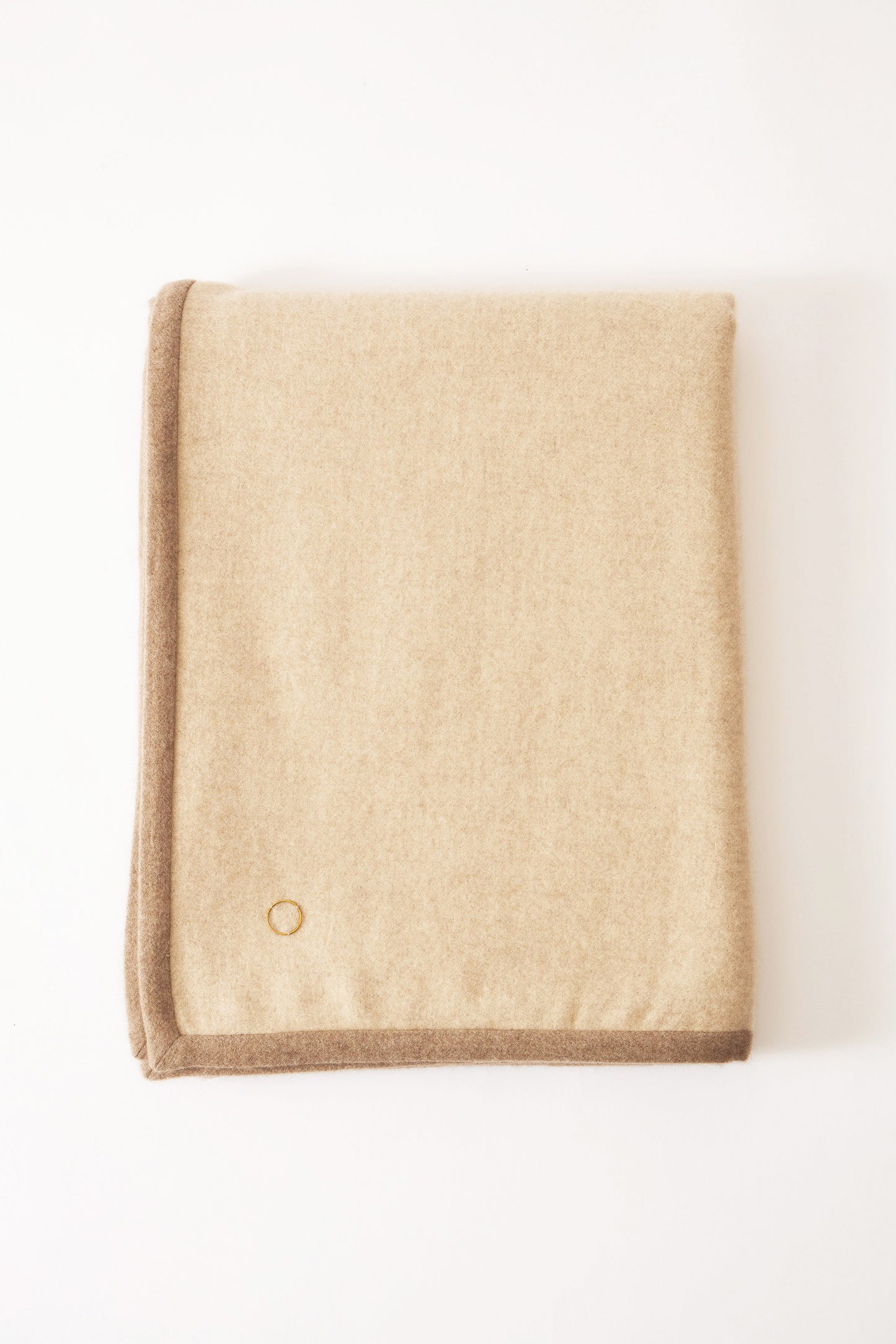 A beige Arteno throw with a subtle pattern and a small circle detail visible on the bottom right corner, displayed on a white background.