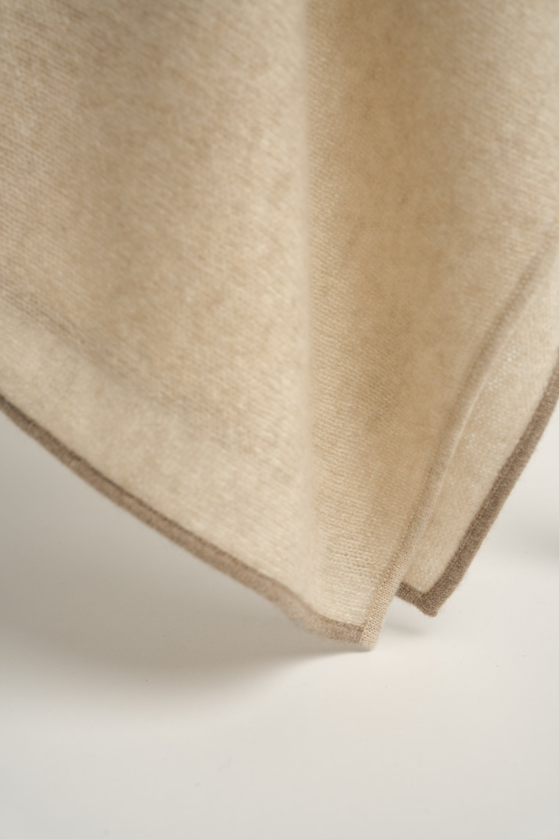 A beige throw with a fine contrast color edge draped over a chair, against a white background.