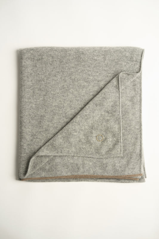 A soft grey throw with a fine contrast color edge draped over a chair, against a white background.