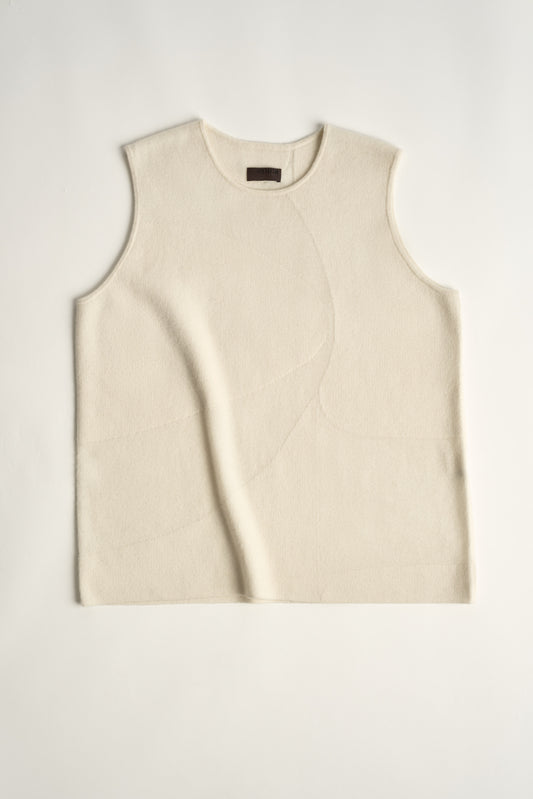 This image features the Duon Top, a stylish and comfortable cashmere knit vest in a subtle ivory color. The vest is designed with a boxy silhouette and fitted shoulders, creating a relaxed yet fitted look.