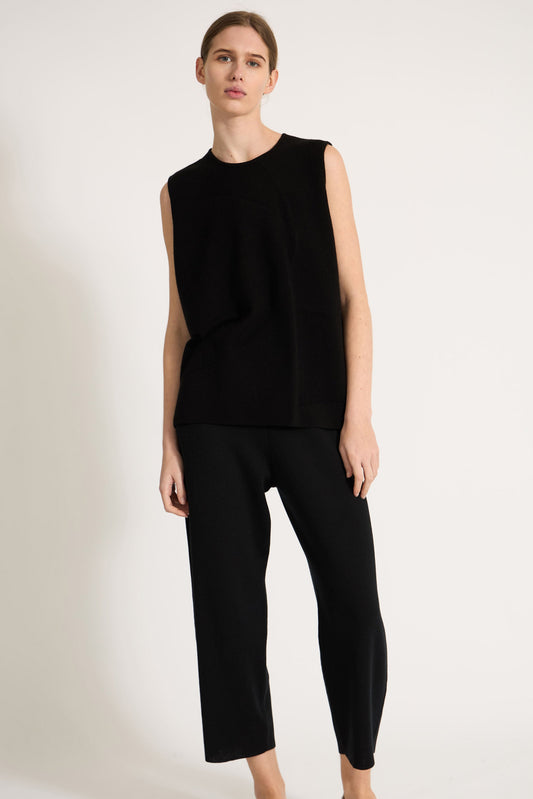 This image features the Duon Top, a stylish and comfortable cashmere knit vest in a subtle black color. The vest is designed with a boxy silhouette and fitted shoulders, creating a relaxed yet fitted look.