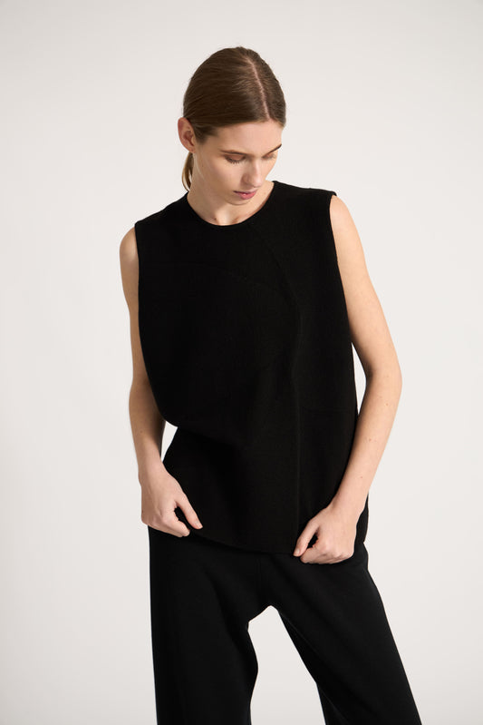 This image features the Duon Top, a stylish and comfortable cashmere knit vest in a subtle black color. The vest is designed with a boxy silhouette and fitted shoulders, creating a relaxed yet fitted look.