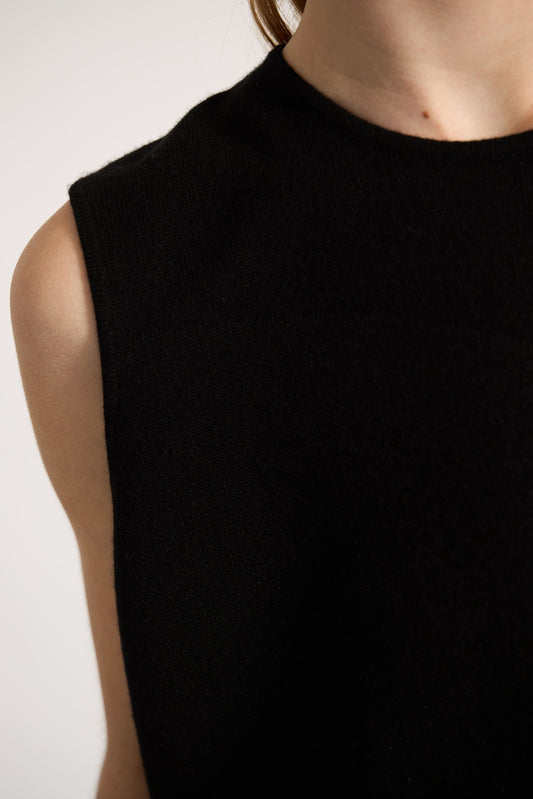 This image features the Duon Top, a stylish and comfortable cashmere knit vest in a subtle black color. The vest is designed with a boxy silhouette and fitted shoulders, creating a relaxed yet fitted look.