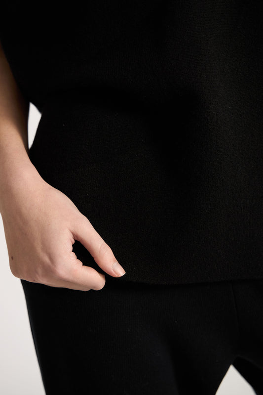 This image features the Duon Top, a stylish and comfortable cashmere knit vest in a subtle black color. The vest is designed with a boxy silhouette and fitted shoulders, creating a relaxed yet fitted look.