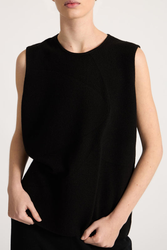 This image features the Duon Top, a stylish and comfortable cashmere knit vest in a subtle black color. The vest is designed with a boxy silhouette and fitted shoulders, creating a relaxed yet fitted look.