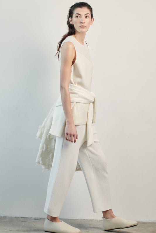 This image features the Duon Top, a stylish and comfortable cashmere knit vest in a subtle ivory color. The vest is designed with a boxy silhouette and fitted shoulders, creating a relaxed yet fitted look.