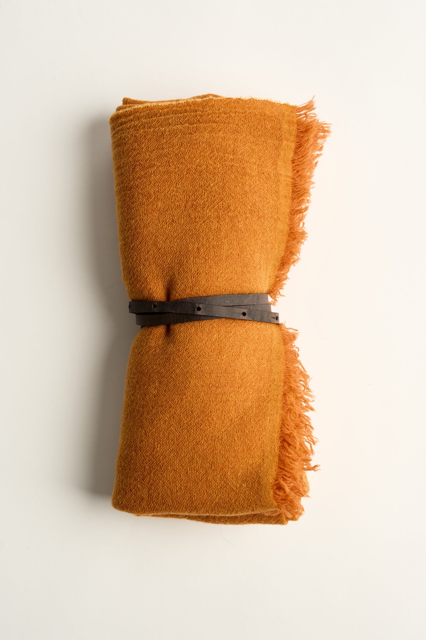 A gold coloured esra throw, tied with a brown leather belt on a white background