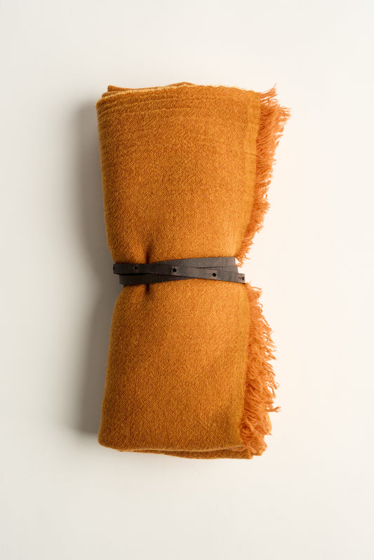 A gold coloured esra throw, tied with a brown leather belt on a white background
