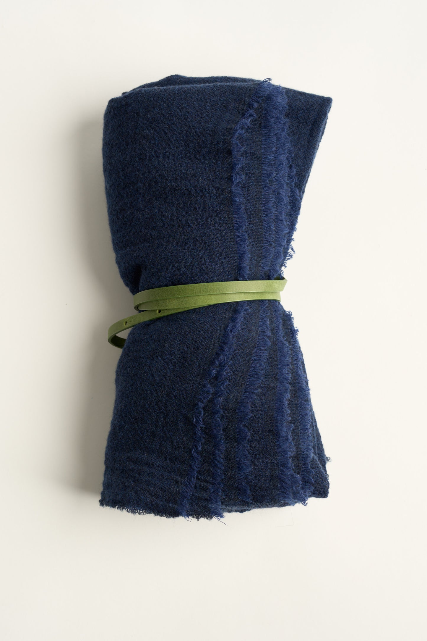 A blue esra throw, tied with a green leather belt on a white background