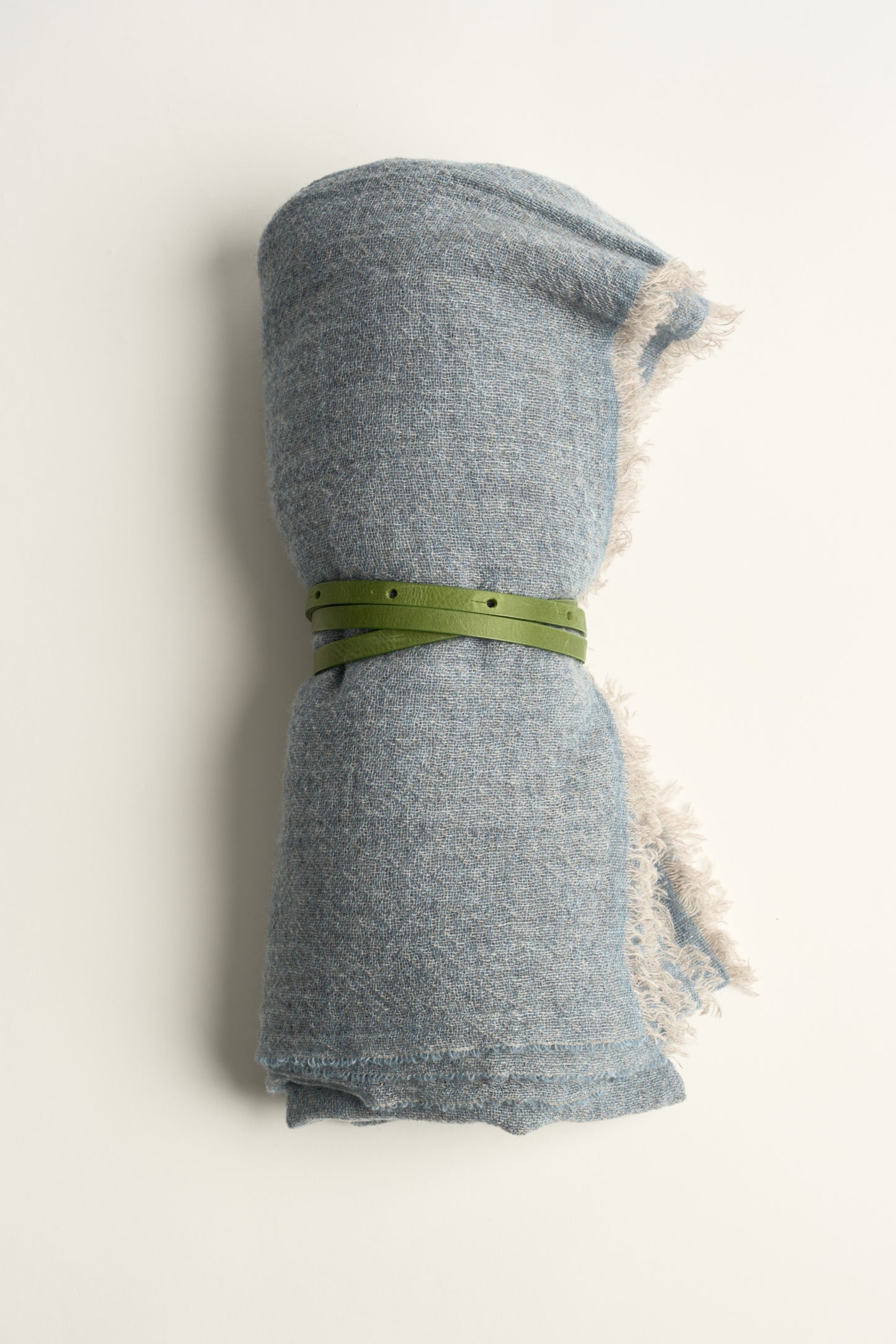 A light soft blue throw with a green leather belt