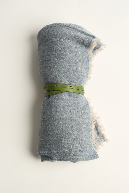 A light soft blue throw with a green leather belt