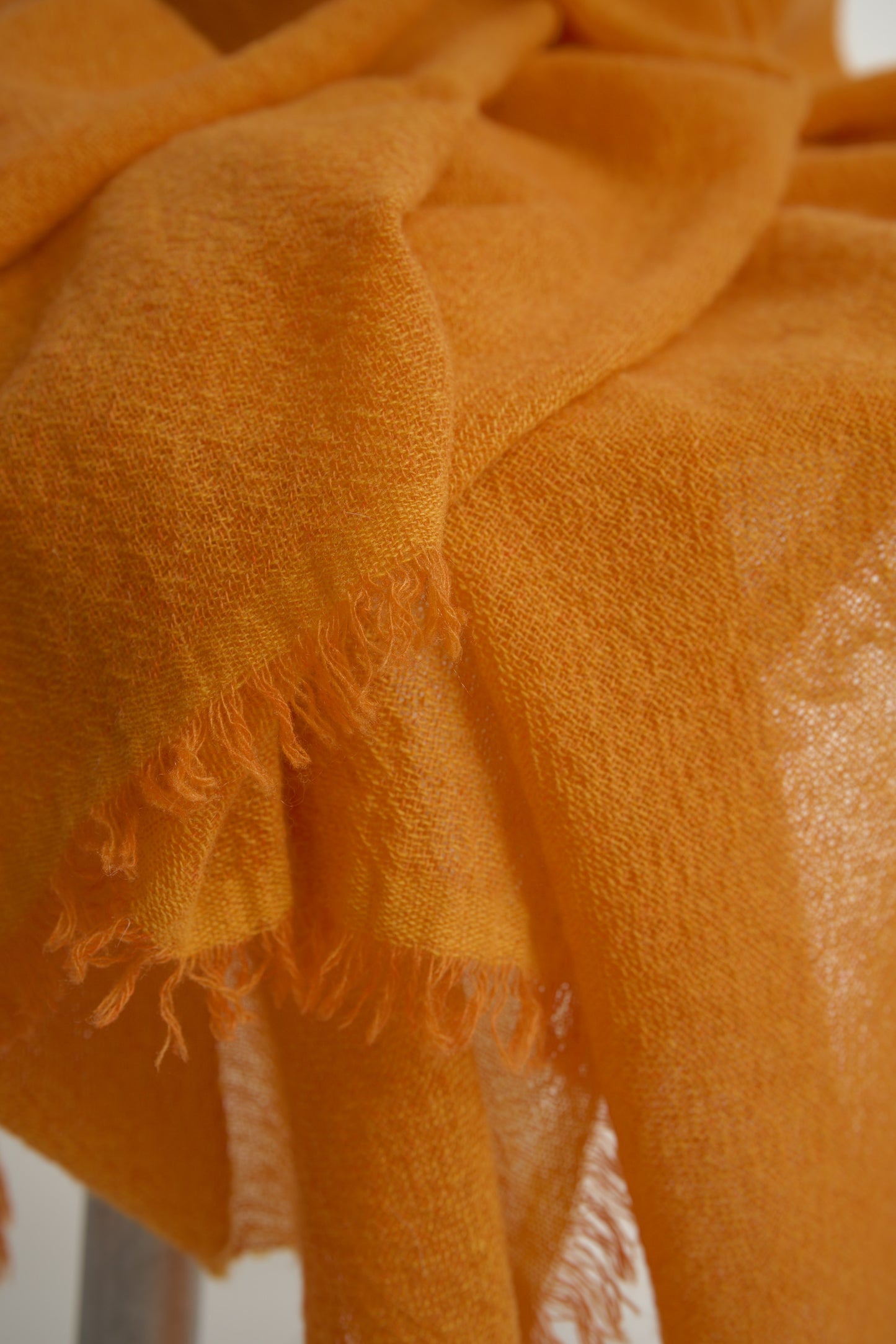 A close up of a vibrant orange cashmere throw with a soft, airy weave, displayed on a chair.