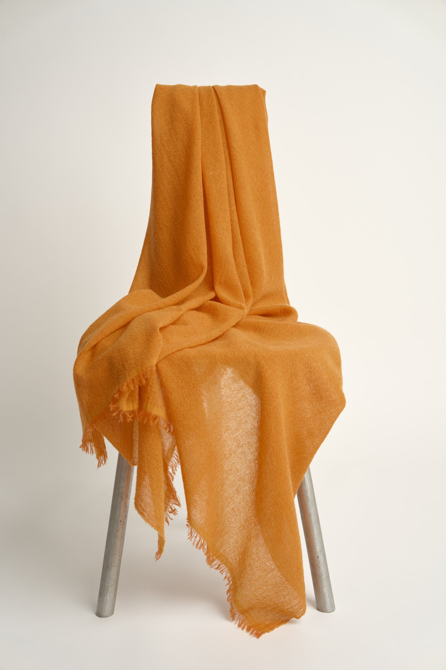 A vibrant orange cashmere throw with a soft, airy weave, displayed on a chair.