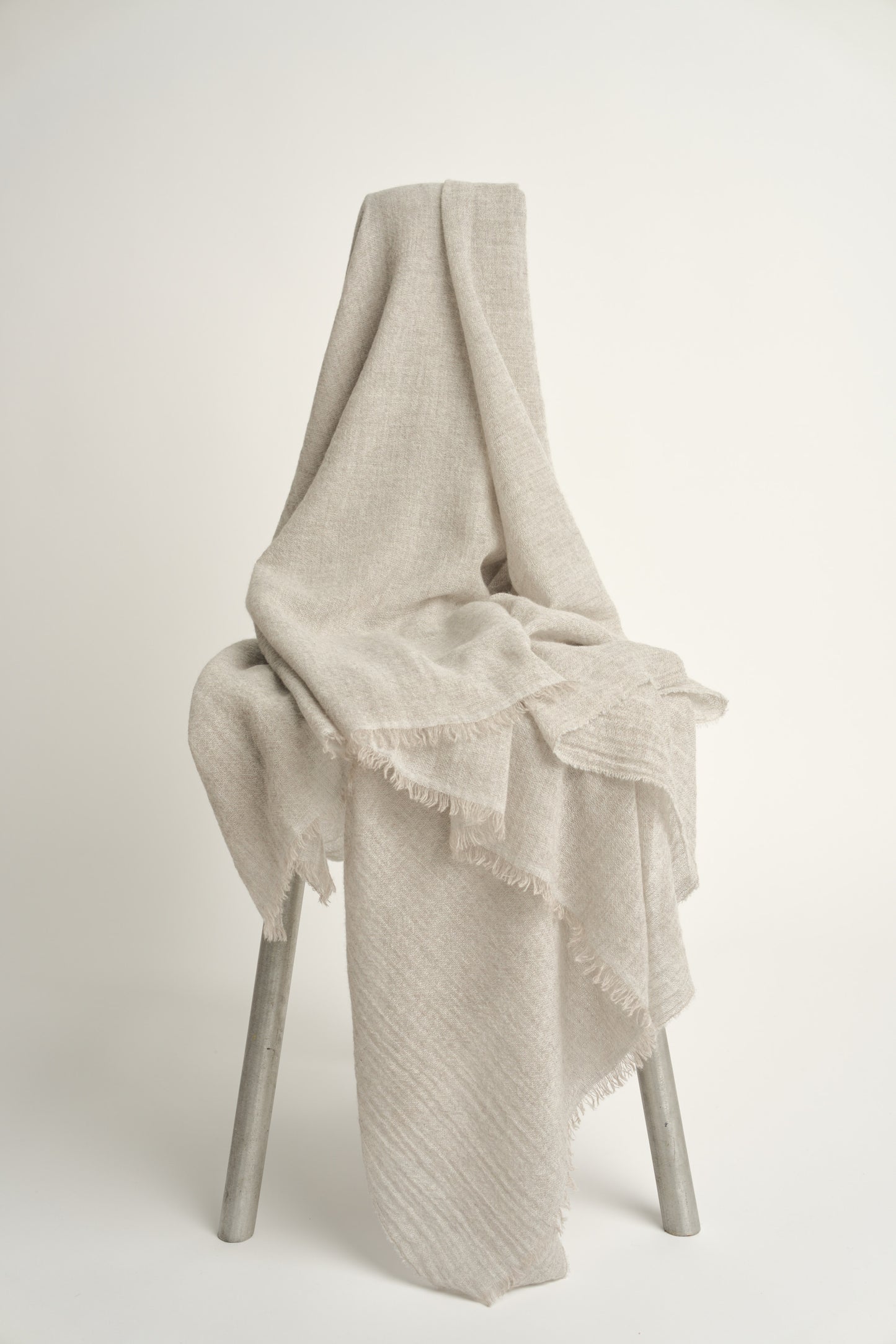 A natural light colour cashmere throw with a soft, airy weave, displayed on a chair.