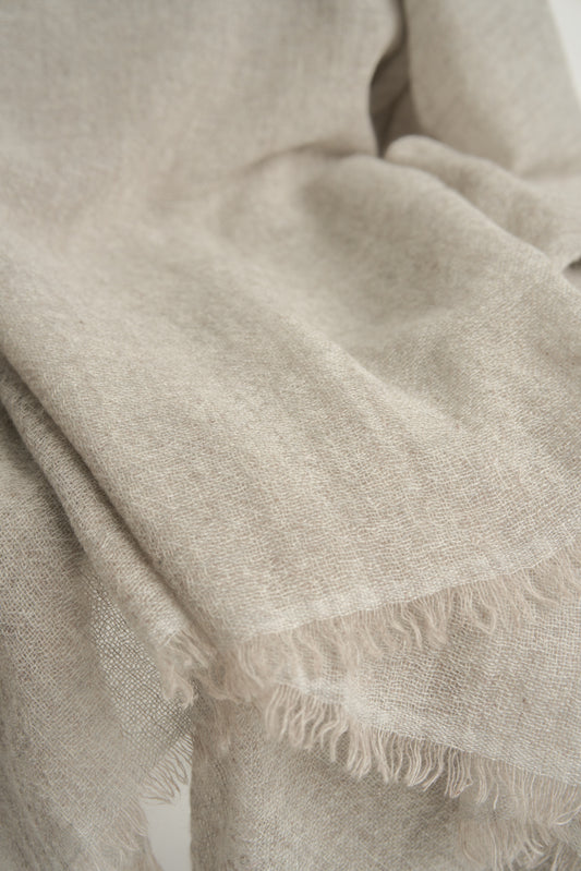 A close up of a natural light colour cashmere throw with a soft, airy weave, displayed on a chair.