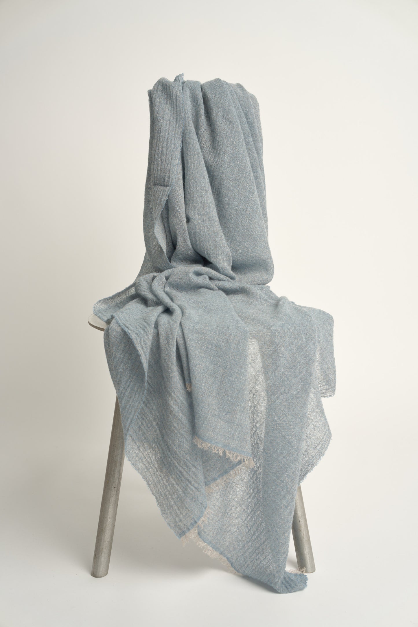 A soft blue cashmere throw with a soft, airy weave, displayed on a plain background on a chair.